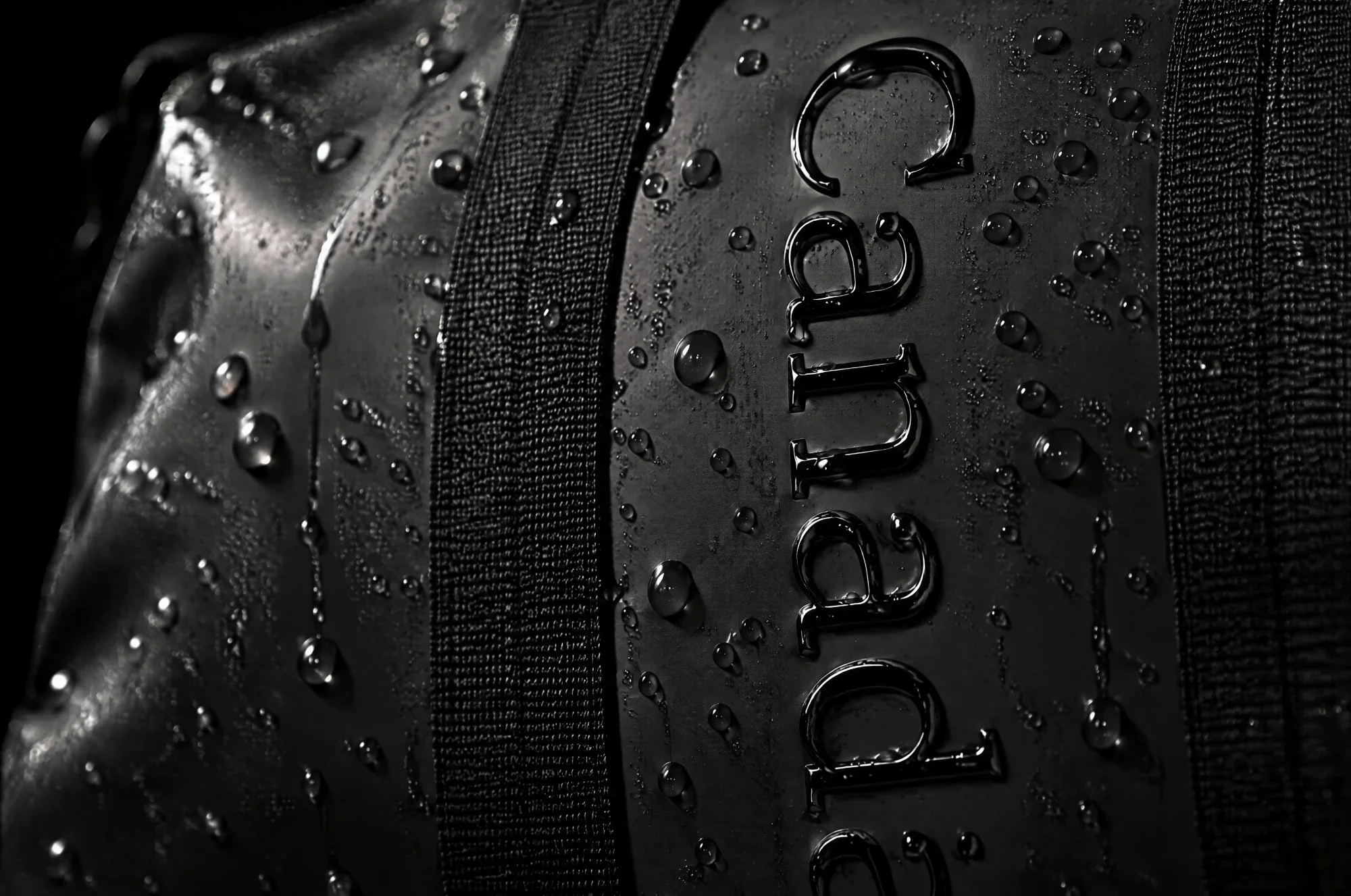 Water beads rolling off the smooth matte surface of the bag around the glossy embossed lettering